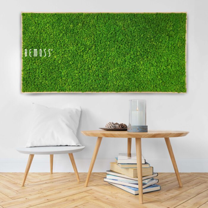 Une chambre minimaliste présente une œuvre d'art murale en mousse verte vibrante sur laquelle figure le mot « BEMOSS ». Ci-dessous, un oreiller blanc repose sur une chaise en bois à côté d’une table ronde en bois contenant des livres et un bougeoir en verre. Le sol est en bois clair avec un motif à chevrons, renforçant l'aspect naturel du tableau de mousse en mousse de RENNE mono.