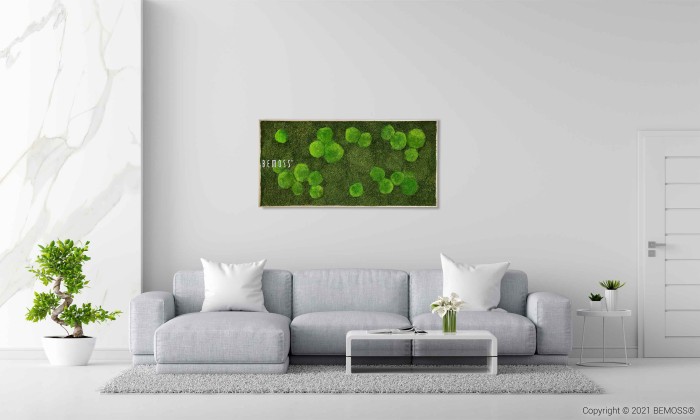 Un salon moderne avec un canapé gris clair, des oreillers blancs et une table basse en verre. Au-dessus du canapé se trouve un Tableau de mousse BEMOSS® ORTHO FOREST accroché au mur. Une plante en pot se trouve à gauche et une porte blanche à droite. La chambre est décorée dans un style minimaliste.