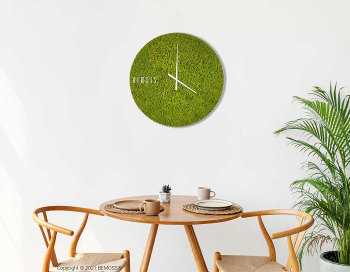 Une salle à manger minimaliste comprenant une table en bois avec deux chaises assorties, un petit plateau avec des tasses et une plante en pot dans le coin. Au mur se trouve une horloge de mousse en mousse de RENNE unique avec des aiguilles blanches et le texte « BEMOSS », ajoutant une touche élégante à l'espace.