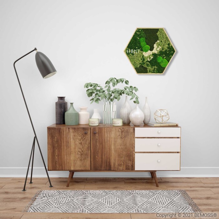 Un buffet en bois moderne avec un mélange de vases verts et blancs et une plante se dresse contre un mur blanc. Au-dessus est accroché un tableau de mousse en forme d'hexagone. Un élégant lampadaire noir avec un abat-jour blanc se trouve à gauche et un tapis à motifs repose sur le sol.