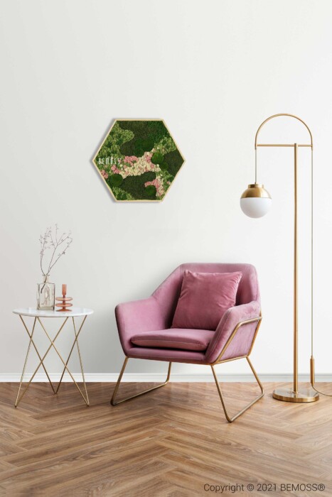 Un coin cosy composé d'une chaise rembourrée rose aux accents dorés, d'une décoration murale hexagonale florale verte réalisée à partir de murs végétaux, d'un lampadaire doré avec un abat-jour sphérique blanc et d'une table d'appoint blanche au décor minimaliste sur un parquet en bois à chevrons.