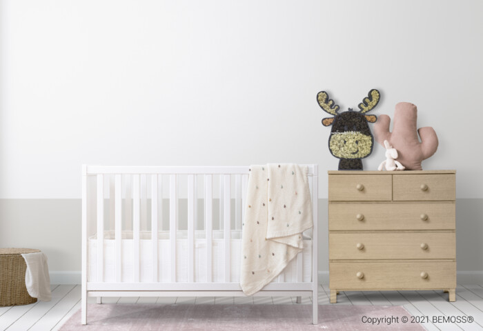 Une chambre de bébé minimaliste comprend un berceau blanc avec une couverture à pois beige, une commode en bois clair avec un animal en peluche et une tête d'orignal décorative sur le dessus. Un panier en osier avec un couvercle repose sur le sol et la pièce présente des murs blancs et gris associés à un parquet en bois et un tableau de mousse BEMOSS.