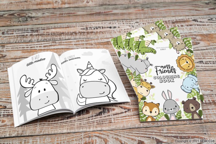 Un livre de coloriage pour enfants intitulé « Forest Friends Coloring Book » est ouvert sur une surface en bois. Une page présente un élan et l'autre une licorne. La couverture du livre met en valeur divers animaux de la forêt, dont un cerf, un ours et un renard parmi des murs végétaux luxuriants.