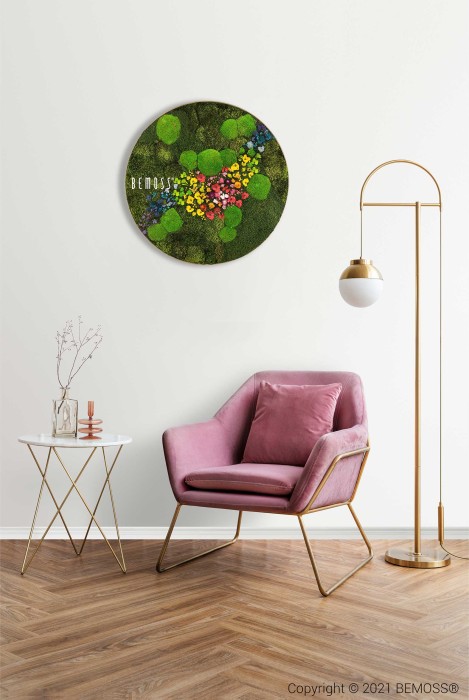 Un salon élégant comprend un fauteuil rose aux pieds dorés à côté d'une table d'appoint ronde blanche contenant des objets décoratifs. Un grand lampadaire avec un abat-jour globe se trouve à proximité. Sur le mur au-dessus de la chaise se trouve un vibrant Tableau de mousse rond PLANTES Arce, créant un tableau de mousse accrocheur avec des accents colorés.