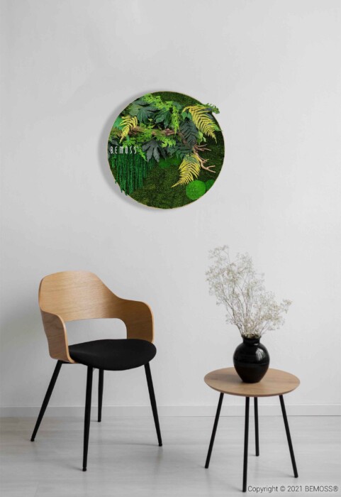 Une pièce minimaliste comprend une chaise en bois avec un coussin noir, une petite table ronde en bois avec un vase noir contenant des fleurs sèches et une décoration murale circulaire BEMOSS avec des plantes et des feuillages verts luxuriants. Le mur blanc et le mobilier simple créent une atmosphère sereine.