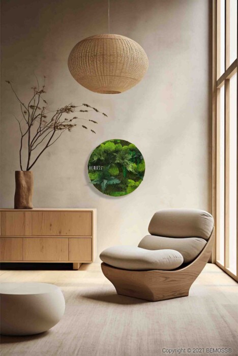 Un salon minimaliste comprend un fauteuil moderne rembourré avec un cadre en bois, un meuble en bois assorti, une grande suspension tissée et une œuvre d'art ronde en mousse verte sur le mur. Des branches nues dans un grand vase ornent le meuble. La lumière filtre à travers une fenêtre.